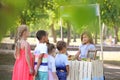 Adorable children waiting in queue for natural lemonade near stand in park