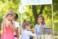 Adorable children waiting in queue for natural lemonade near stand in park