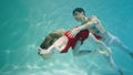 Couple dancing modern choreography underwater. Woman in red costume and man with halfnaked torso gracefully moves in