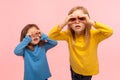 Adorable, curious, nosy two little girls looking through fingers imitating binoculars, exploring world