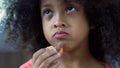 Adorable curly haired girl eating cookie at home, child snacking close-up