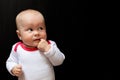 Adorable and cute baby girl with blue eyes and with her finger in the mouth and looking up. Infant on the black Royalty Free Stock Photo