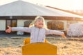 Adorable cute caucasian blond kid girl sitting in wooden cart having fun throwing straw or hay at farm or park during warm autumn