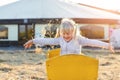 Adorable cute caucasian blond kid girl sitting in wooden cart having fun throwing straw or hay at farm or park during warm autumn