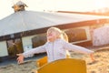 Adorable cute caucasian blond kid girl sitting in wooden cart having fun throwing straw or hay at farm or park during warm autumn