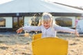 Adorable cute caucasian blond kid girl sitting in wooden cart having fun throwing straw or hay at farm or park during warm autumn