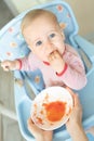 Adorable cute caucasian blond toddler boy eating tasty vegetable soup in chair at kithcen indoor. Mother feeding baby healthy food Royalty Free Stock Photo