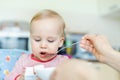 Adorable cute caucasian blond toddler boy eating tasty vegetable soup in chair at kithcen indoor. Mother feeding baby healthy food Royalty Free Stock Photo