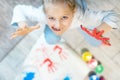 Adorable cute caucasian little blond girl enjoy having fun painting with brush, finger and palm paint at home indoors. Cheerful Royalty Free Stock Photo