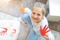 Adorable cute caucasian little blond girl enjoy having fun painting with brush, finger and palm paint at home indoors. Cheerful Royalty Free Stock Photo