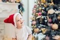 Adorable cute child boy having fun playing at home in red santa claus hat and festive christmas tree on background. Happy toddler Royalty Free Stock Photo