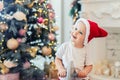 Adorable cute child boy having fun plying at home in red santa claus hat and festive christmas tree on background. Happy Royalty Free Stock Photo