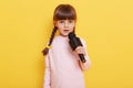 Adorable cute child with microphone in hands singing songs, looks at camera, performing isolated over yellow background, child Royalty Free Stock Photo