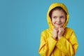 Girl kid wears yellow waterproof raincoat, keeps hands together under chin