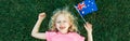 Adorable cute happy Caucasian girl holding Australian flag. Smiling laughing child lying on grass with Australian flag. Kid Royalty Free Stock Photo