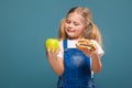 Adorable cute little girl in white shirt and jean jumpsuit with hamburger and apple Royalty Free Stock Photo