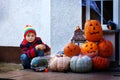 Adorable cute little kid boy sitting with traditional jack-o-lanterns pumpkins for halloween by the decorated scary door