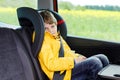 Adorable cute preschool kid boy sitting in car in yellow rain coat. Little school child in safety car seat with belt Royalty Free Stock Photo