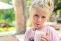 Adorable cute preschooler caucasian blond girl portrait sipping fresh tasty strawberry milkshake coctail at cafe outdoors.