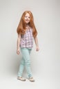 Adorable cute redhead little girl in plaid shirt, bright blue trousers and white boots