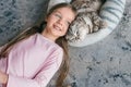 Adorable, cute, smiling girl laying with Scottish gray cat on the carpet at home