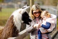 Adorable cute toddler girl and young mother feeding lama and alpaca on a kids farm. Beautiful baby child petting animals Royalty Free Stock Photo