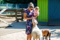 Adorable cute toddler girl and young mother feeding little goats and sheeps on kids farm. Beautiful baby child petting