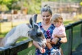 Adorable cute toddler girl and young mother feeding little goats and sheeps on kids farm. Beautiful baby child petting