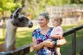 Adorable cute toddler girl and young mother feeding little goats and sheeps on kids farm. Beautiful baby child petting