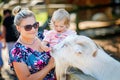 Adorable cute toddler girl and young mother feeding little goats and sheeps on kids farm. Beautiful baby child petting Royalty Free Stock Photo