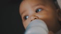 Adorable dark skin multiracial baby drinking his formula milk from the bottle in the hands of his mom Royalty Free Stock Photo