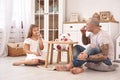 Adorable daughter wearing a white dress whith her loving father. They are drinking tea from a toy dishes in a modern kid