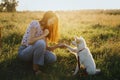 Adorable fluffy puppy giving paw to girl owner and having treat. Woman training cute white puppy to behave in summer meadow in
