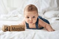 Adorable four month old baby boy in denim dungarees lying on white bed Royalty Free Stock Photo