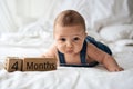 Adorable four month old baby boy in denim dungarees lying on white bed Royalty Free Stock Photo