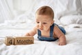 Adorable four month old baby boy in denim dungarees lying on white bed Royalty Free Stock Photo