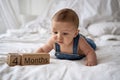 Adorable four month old baby boy in denim dungarees lying on white bed Royalty Free Stock Photo