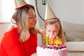 Adorable four years old european blonde girl makes a wish before blowing out the candles on a birthday cake that mom is holding Royalty Free Stock Photo