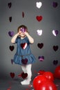 Adorable funny white Caucasian little girl toddler in studio with red balloons hearts on grey background making faces having fun Royalty Free Stock Photo