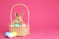 Adorable furry Easter bunny near wicker basket with dyed eggs on color background Royalty Free Stock Photo