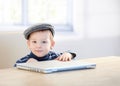 Adorable ginger boy in cap playing with laptop