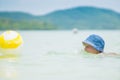 Adorable girl in blue hat swim in ocean near beach. Play with ye