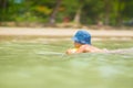 Adorable girl in blue hat swim in ocean near beach. Play with ye