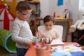 Adorable girl and boy sitting on table cutting paper at kindergarten