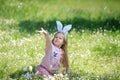 Adorable girl with bunny ears having fun at Easter egg hunt in meadow with first spring flowers. Kid with long blond Royalty Free Stock Photo