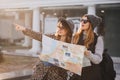 Adorable girl in gray knitted hat walking with friend around city and holding map. Outdoor portrait of two charming