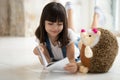 Adorable girl laying on warm floor with favorite toy, reading. Royalty Free Stock Photo