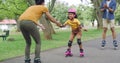 Adorable girl learning to rollerskate with parents cheering, encouraging and supporting her. Cute little latino learning