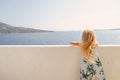 Adorable girl with long blond hair and summer dress looking from the balcony