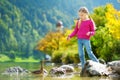 Adorable girl playing by Konigssee lake in Germany on warm summer day. Cute child having fun feeding ducks and throwing stones int Royalty Free Stock Photo